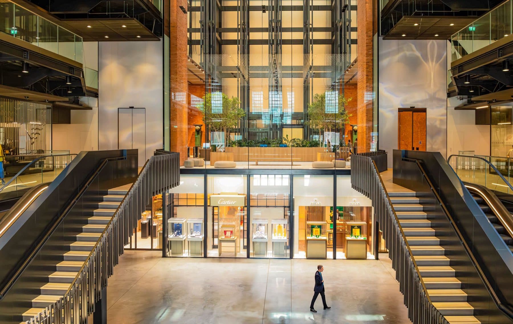 The restored interior of Battersea Power Station: twin staircases and escalators either side of a glass-fronted jewellery hall, brick columns rising several storeys above.